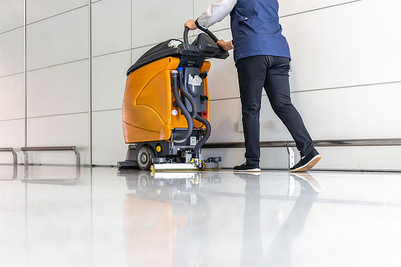 Reinigungskraft mit Scheuersaugmaschine auf glänzendem Boden